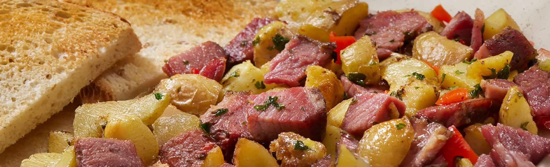 Corned beef hash with diced potatoes, red peppers, and herbs, served with two slices of toasted bread on the side.