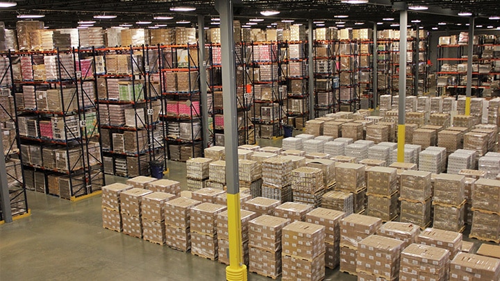 Spacious warehouse with tall shelves stacked with boxes, pallets, and organized cartons ready for shipping or storage.
