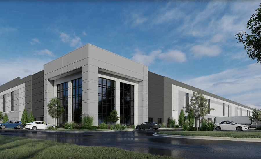 Modern industrial or office building with tall windows, landscaped greenery, parked cars, and a partly cloudy blue sky.